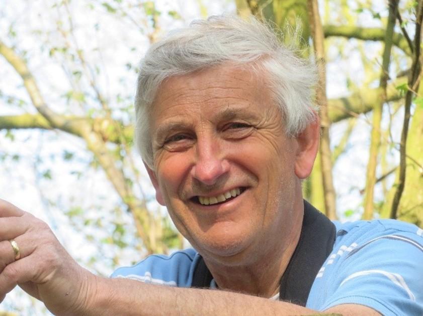 Man in woodland area wearing blue polo shirt and smiling at the camera